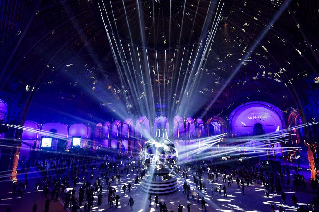 People skate on the indoor ice rink at the Grand Palais des Glaces, in Paris. A large reflective ball stands in the centre, with lights shining on to it from the walls and roof of the building.