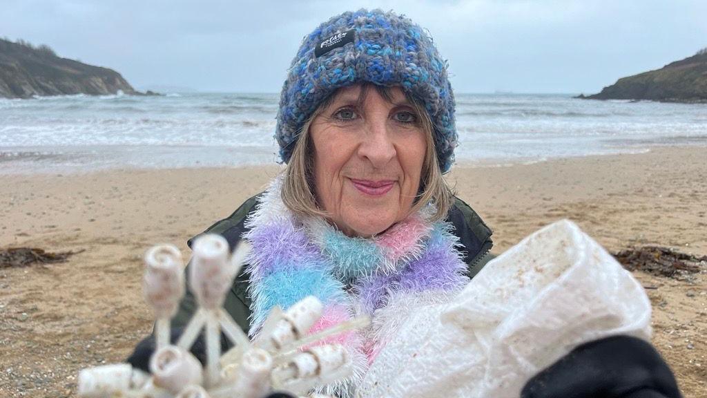 A picture of a woman holding plastic on a beach.