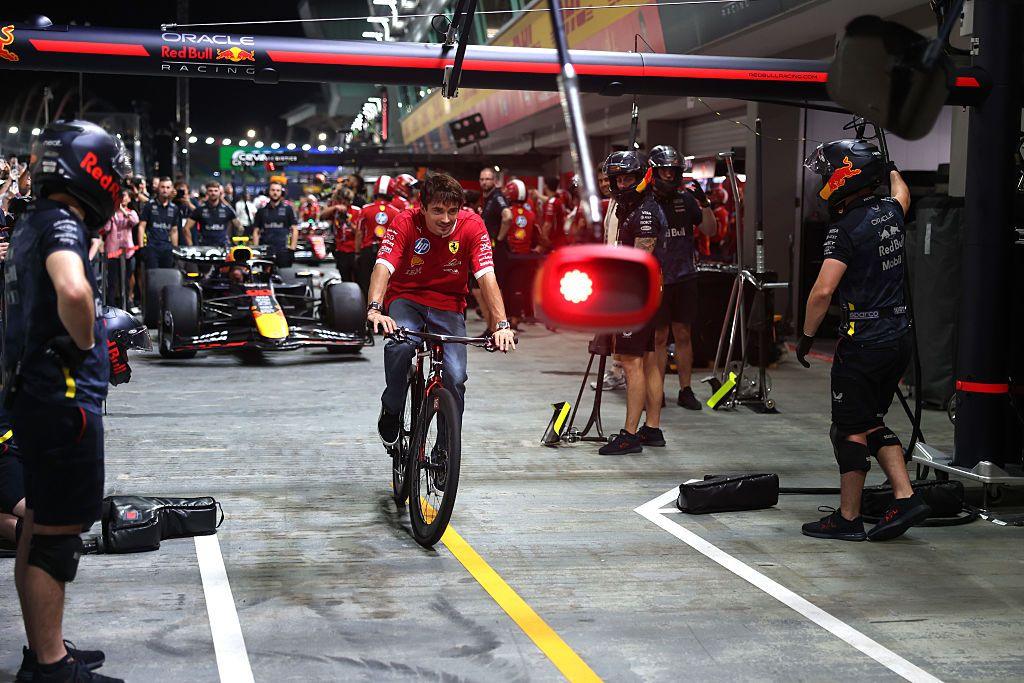 Ferrari's Charles Leclerc cycling through the pit lane at the Singapore Grand Prix with a Red Bull F1 car in the background