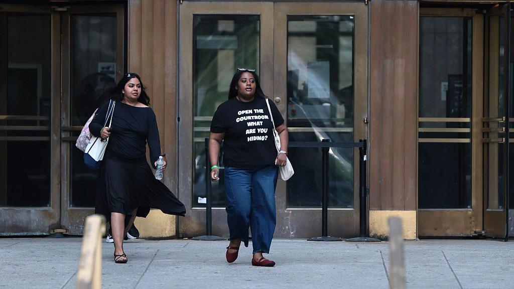 Public spectators leave Mangione's hearing. A woman wears a shirt that says, "Open the courtroom, what are you hiding?"