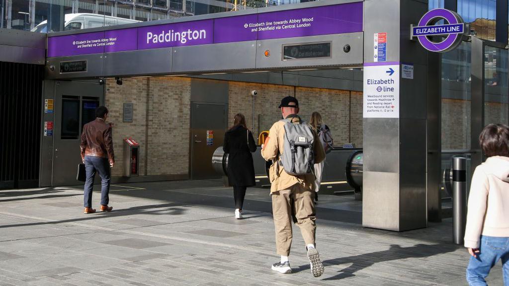 A file image showing people walking under purple signage and an Elizabeth Line roundel towards escalators at an entrance to Paddington Station