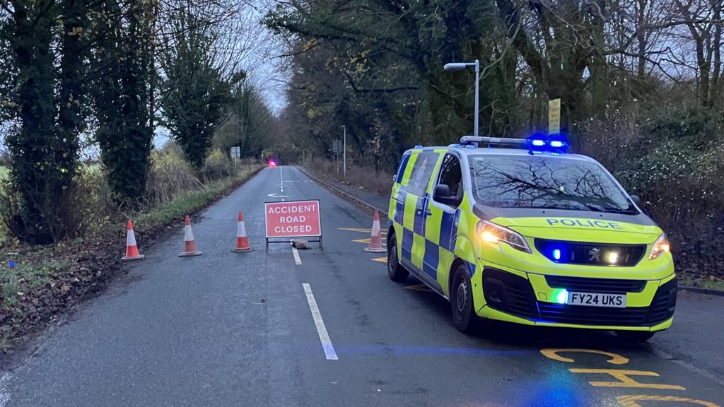 A police van parked in front of a cordon with a road closure sign in place.