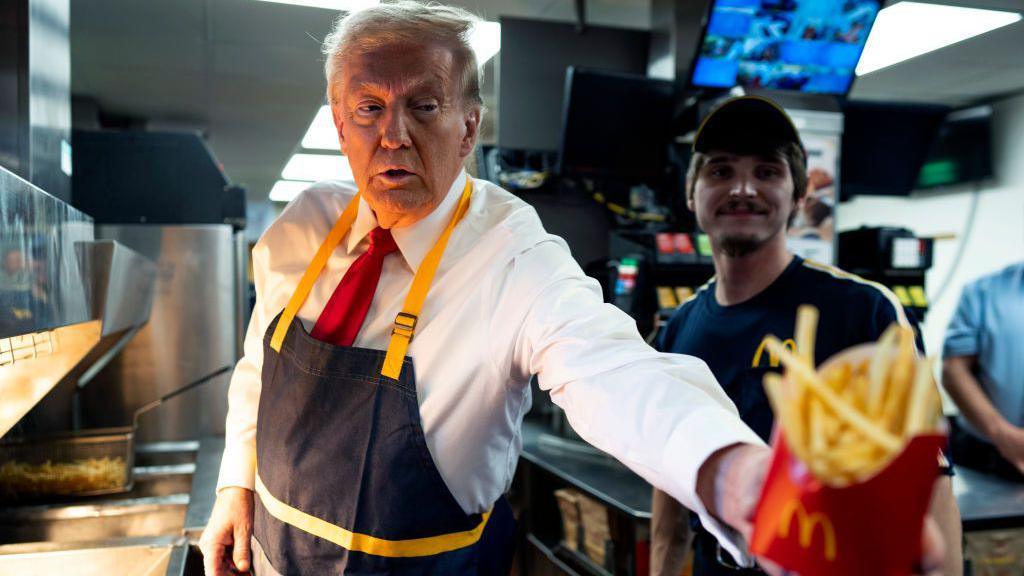 Donald Trump, wearing a white shirt, red tie and a dark blue apron with yellow details, works behind the counter during a campaign event at McDonald's restaurant on 20 October, 2024 in Feasterville-Trevose, Pennsylvania.