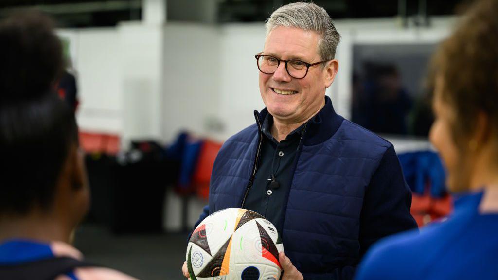 Labour leader Sir Keir Starmer holds a football while talking with members of the women's under-17 England team