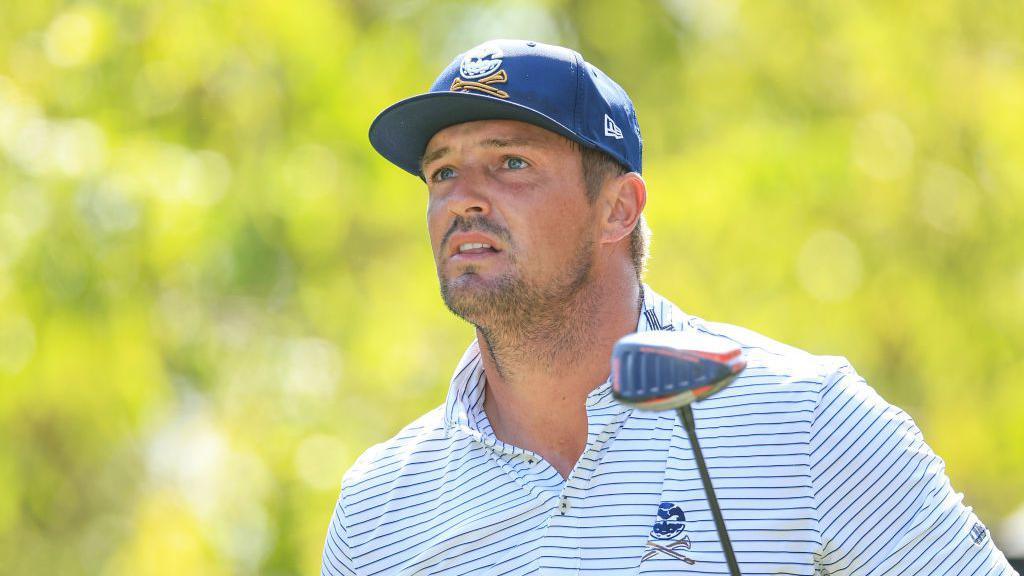 Bryson DeChambeau wearing a blue cap. white T-shirt with blue stripes and holding a driver