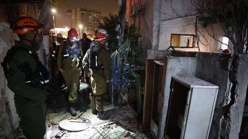 Crews check damage of an Iranian building after strikes. They are wearing hard-hats and you can see exposed wires and brick