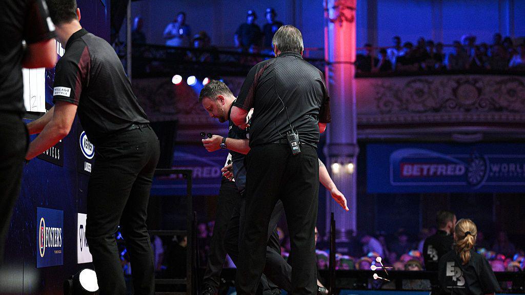 Cameron Menzies is helped by darts officials on stage