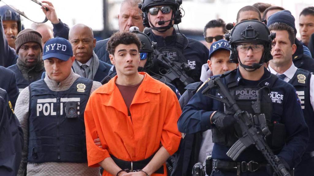 Luigi Mangione, the suspect in the murder of UnitedHealth Group executive Brian Thompson, arrives at a helicopter pad after being extradited from Pennsylvania, as Mayor Eric Adams walks behind him, in New York