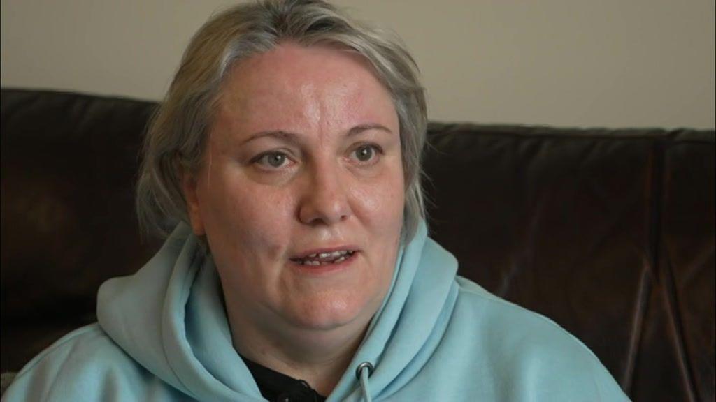 A woman with short blond hair and a pale blue hoodie on a dark sofa