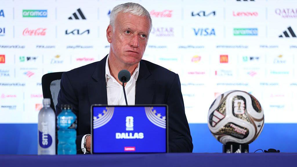 Didier Deschamps sits behind a microphone during a press conference in Dallas