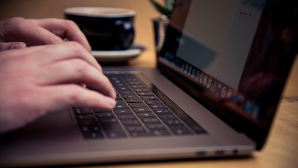 Two hands are typing on the keyboard of an open silver laptop