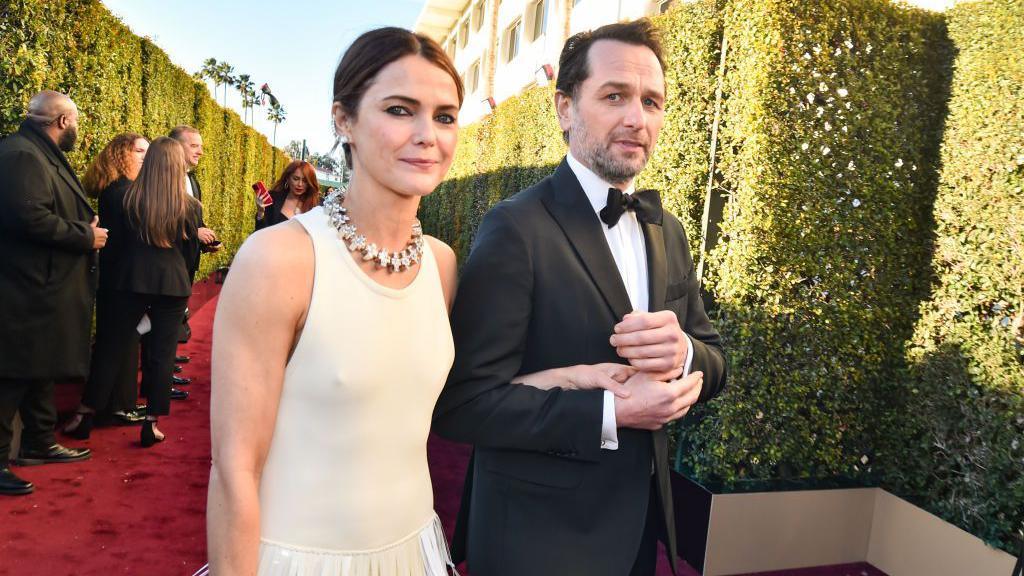 Keri Russell, left, and Matthew Rhys at the 81st Golden Globe Awards held at the Beverly Hilton Hotel on January 7, 2024 in Beverly Hills, California.
She is wearing a white dress and necklace, he is in a black dinner suit and bowtie.