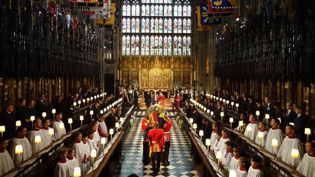 The funeral of Queen Elizabeth II in Westminster Abbey. Pallbearers are carrying the coffin down the aisle with choirs on either side.