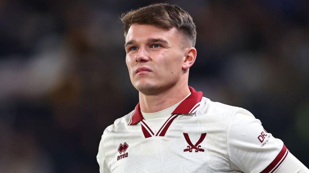 Jamie Shackleton, who is wearing a predominantly white Sheffield United jersey with red trim, including a red logo of two swords crossing.