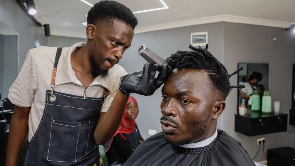 A barber cuts a client's hair at the re-opening of a barber shop in Nairobi, Kenya - Friday 7 March 2025