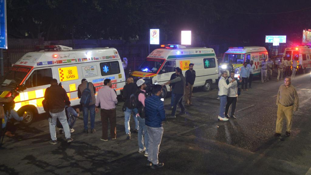 A crowd of people stand in the road in front of a row of ambulances