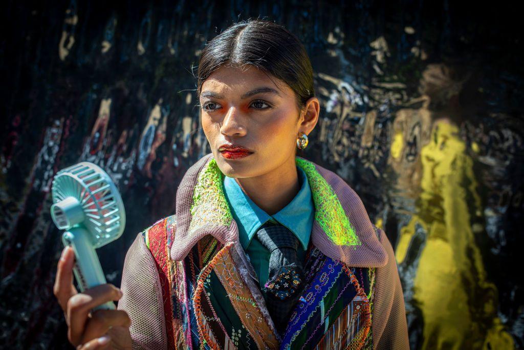 A model wearing a multicolour, multi-textured coat in South African summer cools herself with a hand-held fan.