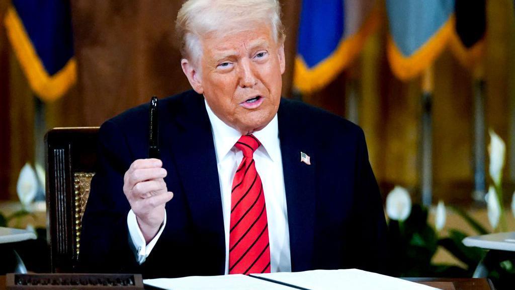 President Donald Trump waves a pen sitting at a desk when signing an executive order to largely dismantle the Education Department on 20 March 2025