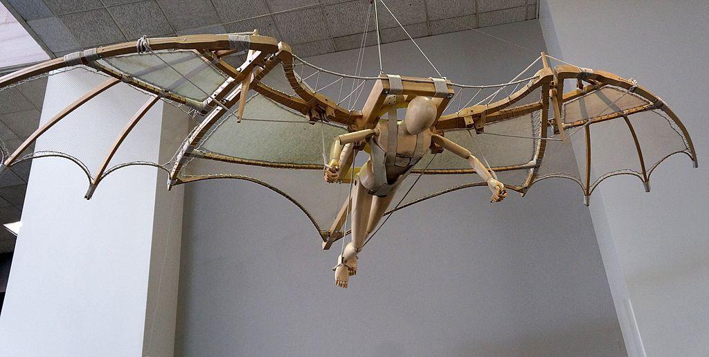 A model of Leonardo Da Vinci's wooden flying machine suspended from a white tiled ceiling.