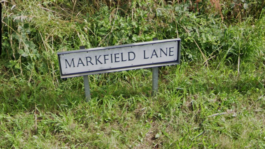 A street sign saying Markfield Lane with grass around the sign