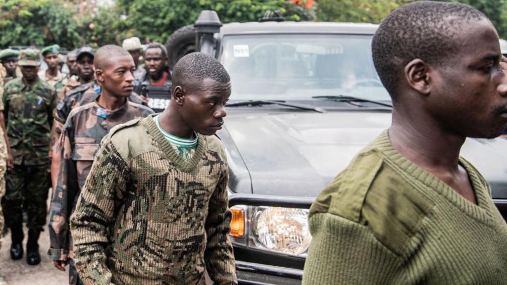 Image of alleged members of the Democratic Forces for the Liberation of Rwanda (FDLR), wearing military outfits of different patterns with a car in the background