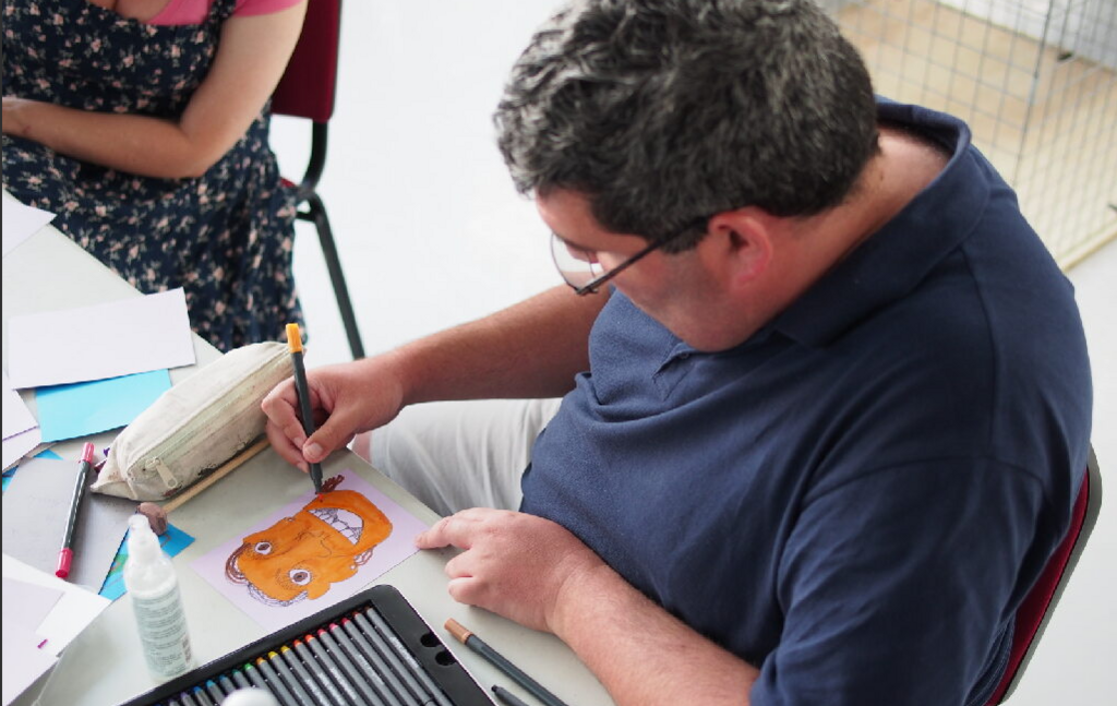 Man in a navy top using a felt tip pen to colour a portrait