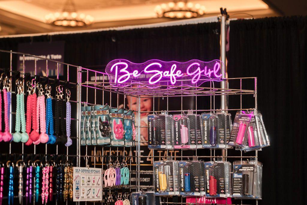 A neon sign says "Be Safe Girl" and advertises rainbow-hued self-defense products like rape whistles