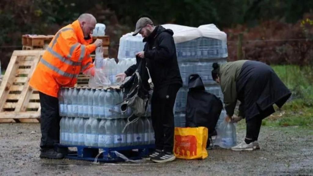 A man in hi vis jacket standing in a car park with a lot of bottles of water 