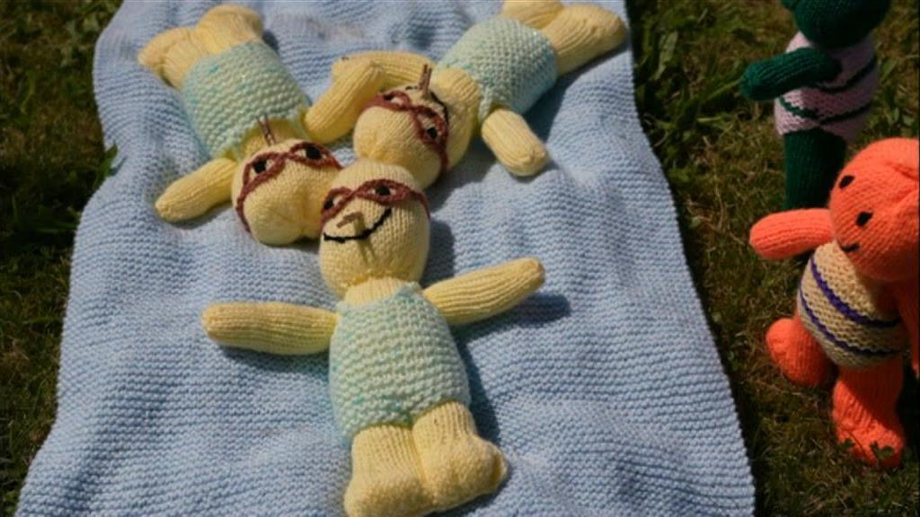 Three knitted figures lie on a blue towel as if they are swimming in sync.