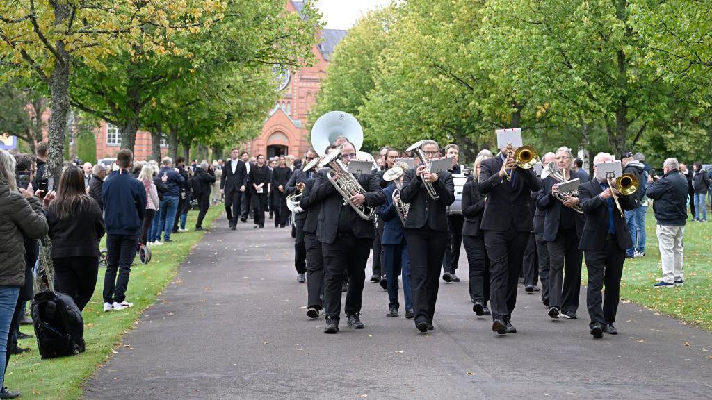 A brass band lead mourners out of the church