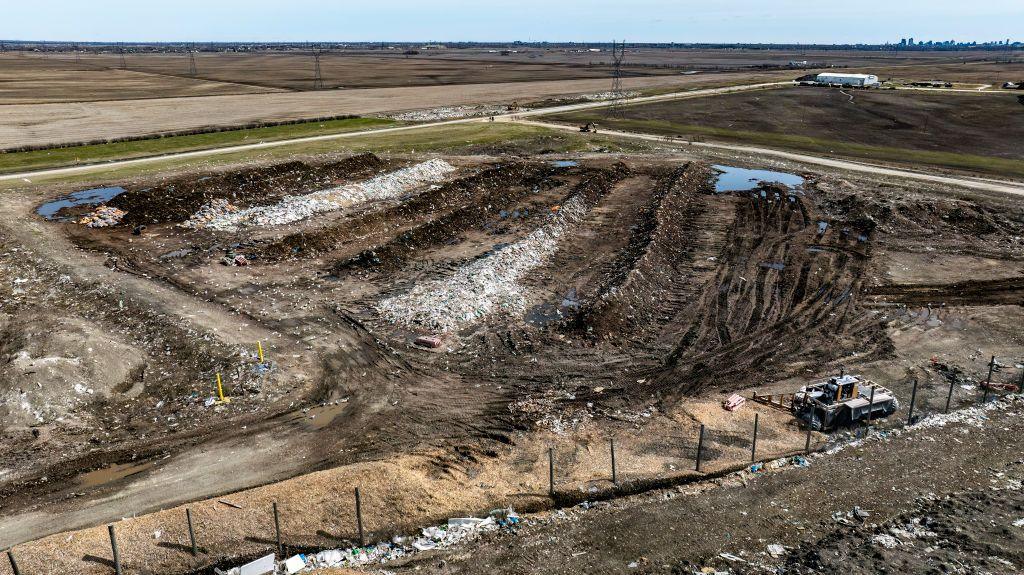 The Prairie Green Landfill is a large patch of dirt. Theres a truck, and white garbage bags, and tyre marks that have formed trenches in the dark dirt