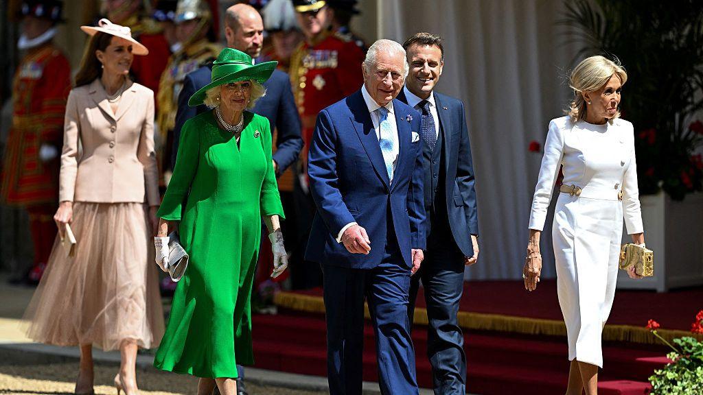 Princess of Wales, Princes of Wales, Queen Camilla, King Charles, Emmanuel Macron and Bridget Macron walking alongside a red carpet 