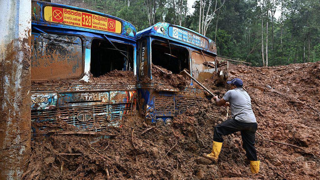 A worker removes mud accumulated around buses near a landslide-affected area in the aftermath of Cyclone Ditwah, in Maspanna on December 13, 2025.