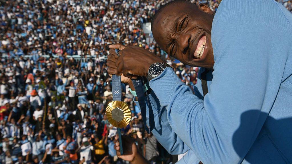 An image of Botswana athlete Letsile Tebogo holding his gold medal as people cheer him on