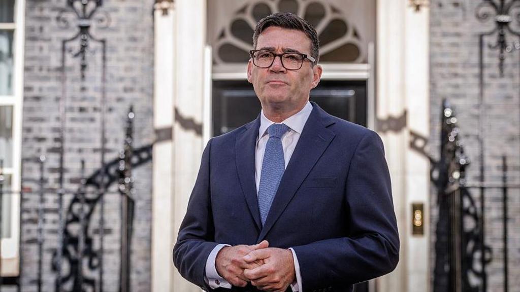 Burnham holds his hands together in front of him as he looks solemn 