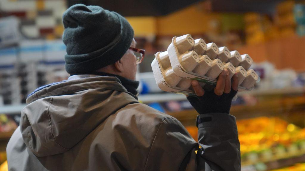 A customer, holding a carton of eggs, is seen during shopping at a supermarket as packages of eggs are seen on the shelves of the egg aisle in New York City, United States on December 20, 2024. 