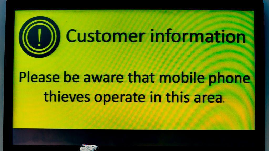 Sign saying "Please be aware that mobile phone thieves operate in this area". 