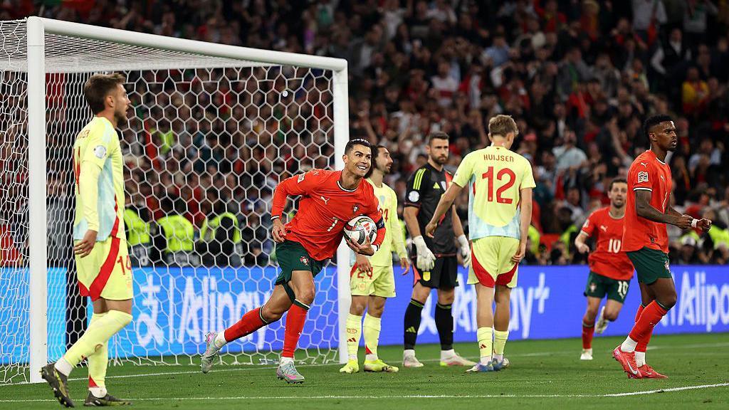 Ronaldo smiling and holding the ball after scoring a goal.