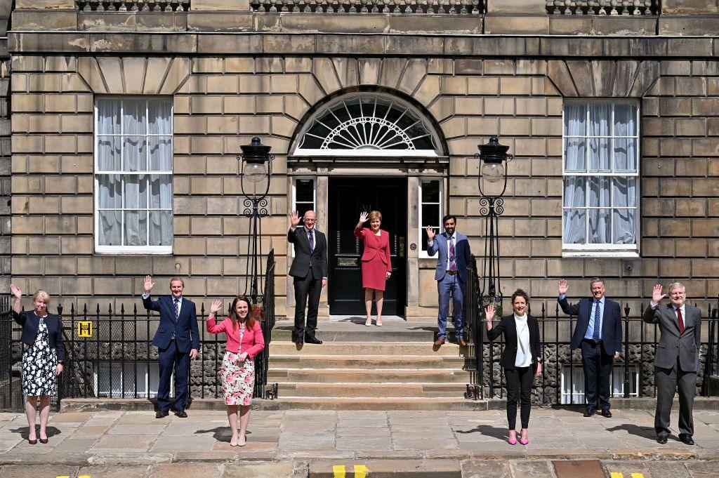 A picture from 2021 of Nicola Sturgeon's cabinet, waving from the steps of Bute House. From left they are Shona Robison (leaving), Michael Matheson (leaving), Kate Forbes (leaving), John Swinney (standing), Nicola Sturgeon (leaving), Humza Yousaf (leaving), Mairi Gougeon (leaving), Keith Brown (standing) and Angus Robertson (standing)