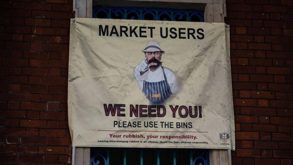 A sign displayed at Smithfield Market urging people to use the rubbish bins. In a play of Lord Kitchener's war poster "Your Country Needs You" - a moustachioed man pointing at the viewer - the sign has a man wearing a butcher's outfit and the slogan says "We Need You, please use the bins"