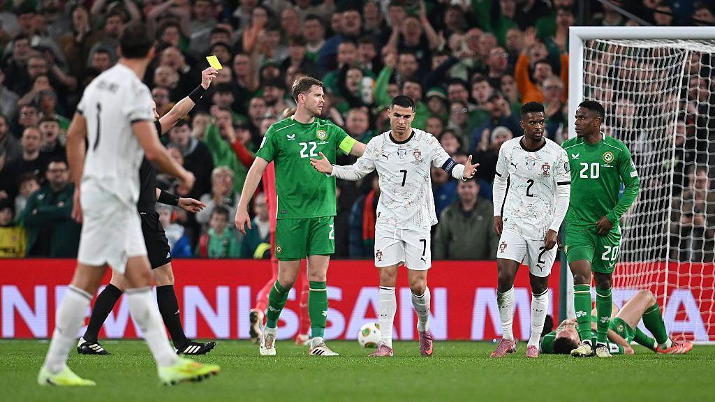 Cristiano Ronaldo is shown a yellow card after elbowing Dara O'Shea who is lying on the floor