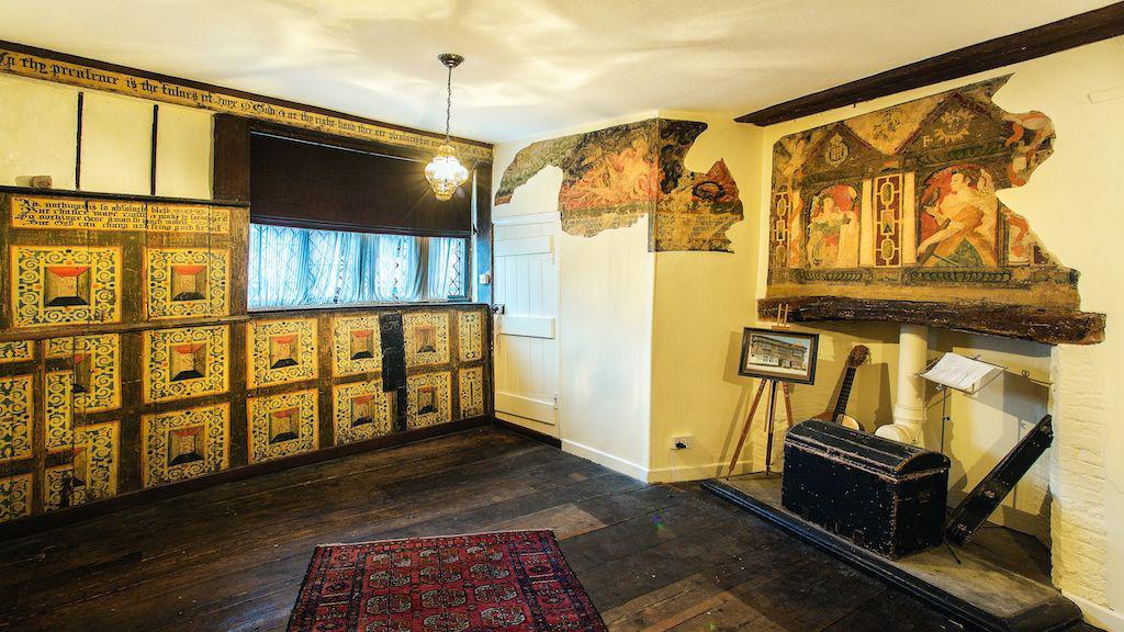 A small room with wooden flooring and white walls. Some of the walls show old paintings of what look to be women.