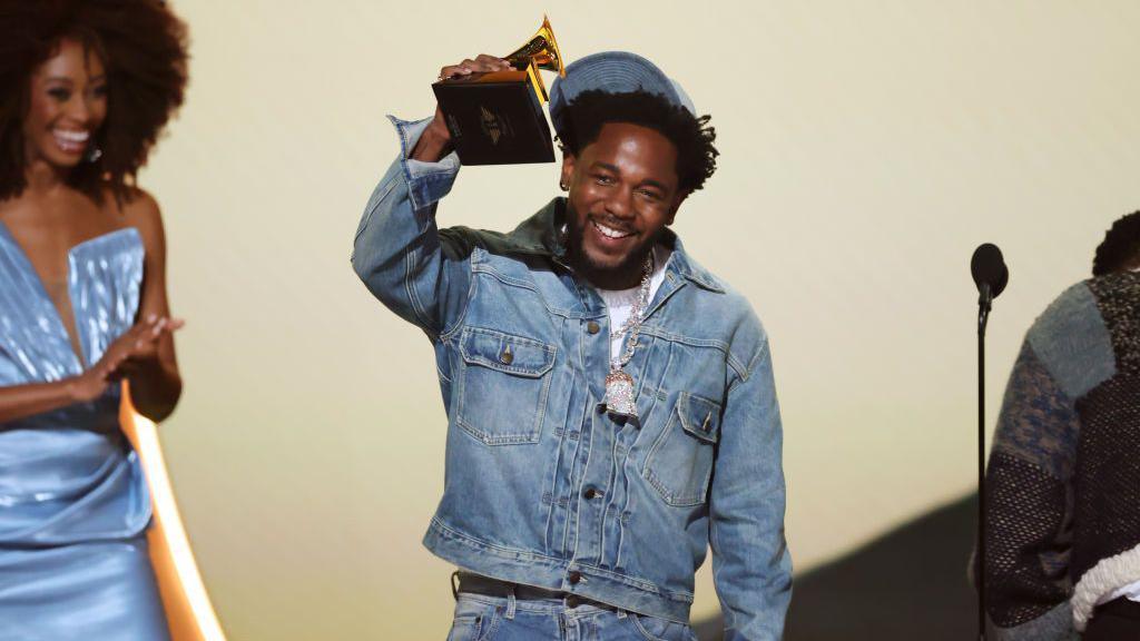 Kendrick Lamar stands on stage at the Grammys and holds up his award after winning for record of the year with his diss track Not Like Us 