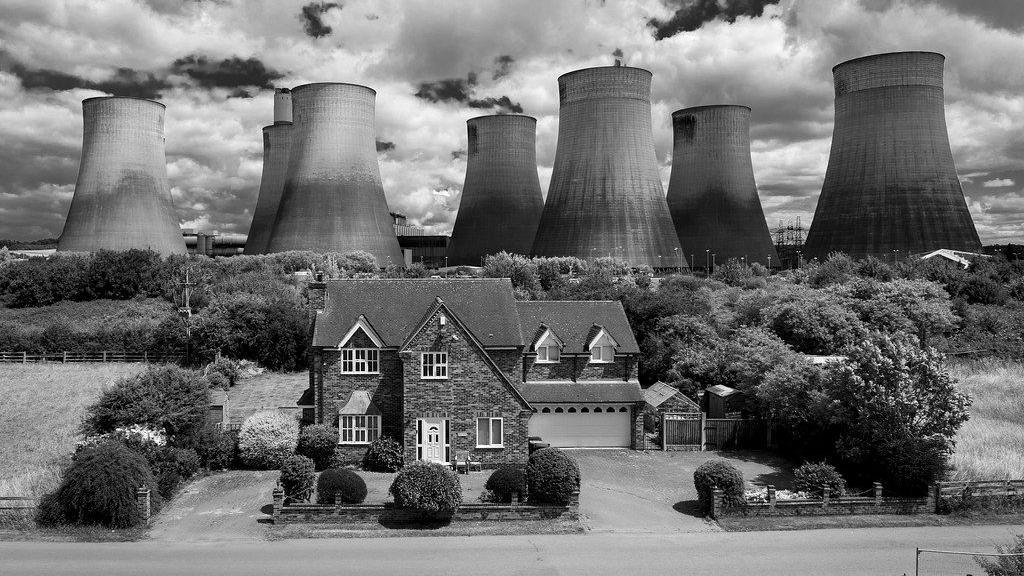 A house in front of Ratcliffe-on-Soar power station's cooling towers in black and white.