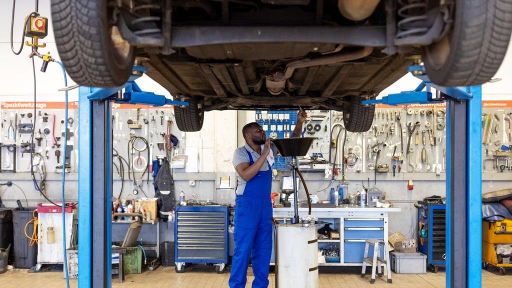 A mechanic opens the oil drain plug of a car