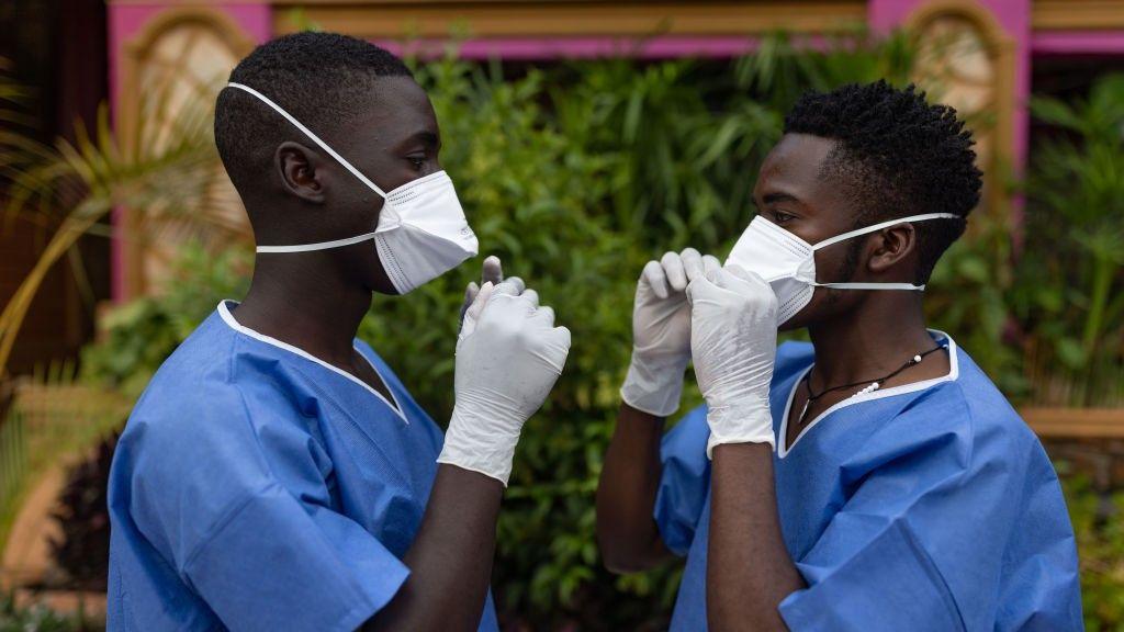 Two men wearing protective gear face each other while adjusting their masks