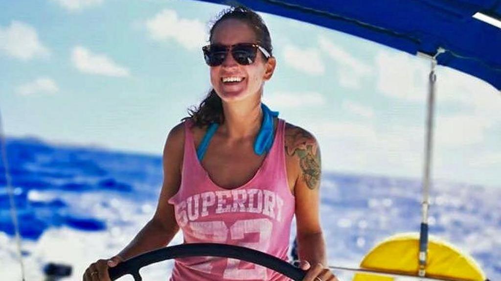 Picture of Sarm Heslop at the wheel of a yacht. She is wearing a turquoise halter-neck bikini and a pink vest with a white Superdry logo. Her dark hair is tied back and she is wearing sunglasses and smiling. Behind her is a blue ocean and blue sky.