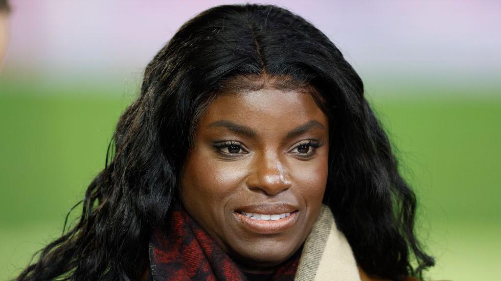 Eni Aluko smiles on the touchline while conducting punditry for TNT Sports during a Premier League match