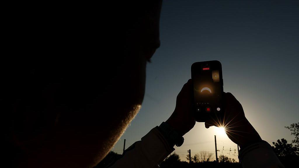 A sporting fan takes a video of the eclipse on his phone