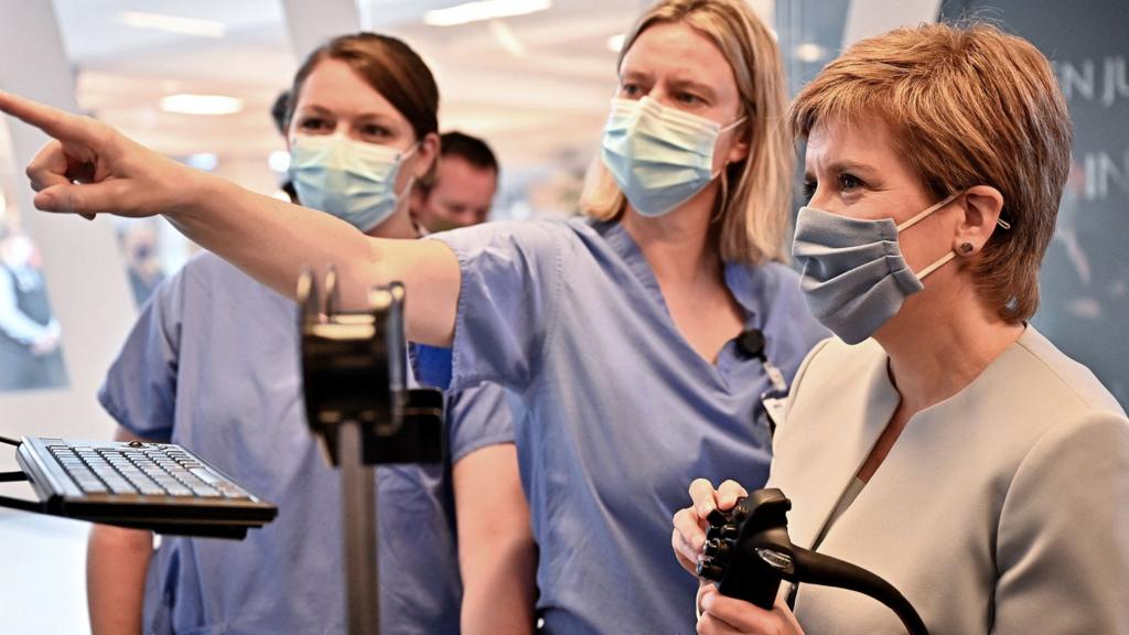 Scotland's First Minister Nicola Sturgeon (R) gestures as she tours a mock theatre set up with innovative new medical equipment, including robotic surgery devices, during a visit to launch the NHS recovery plan at the new national Centre for Sustainable Delivery (CfSD) at the Golden Jubilee Hospital in Clydebank, Scotland, on August 25, 2021.